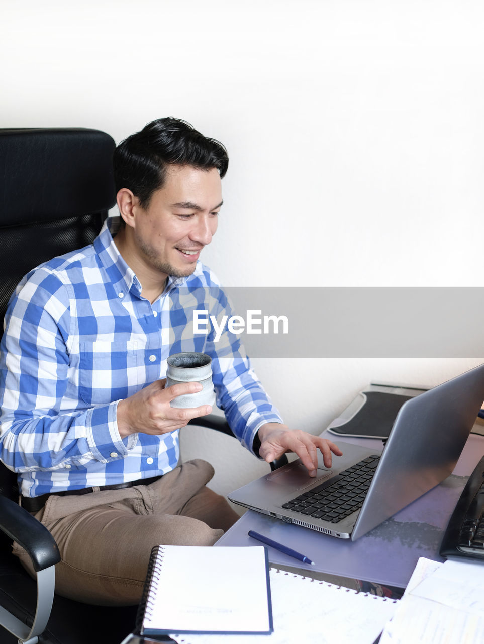 A man in a checked shirt working from home at a desk