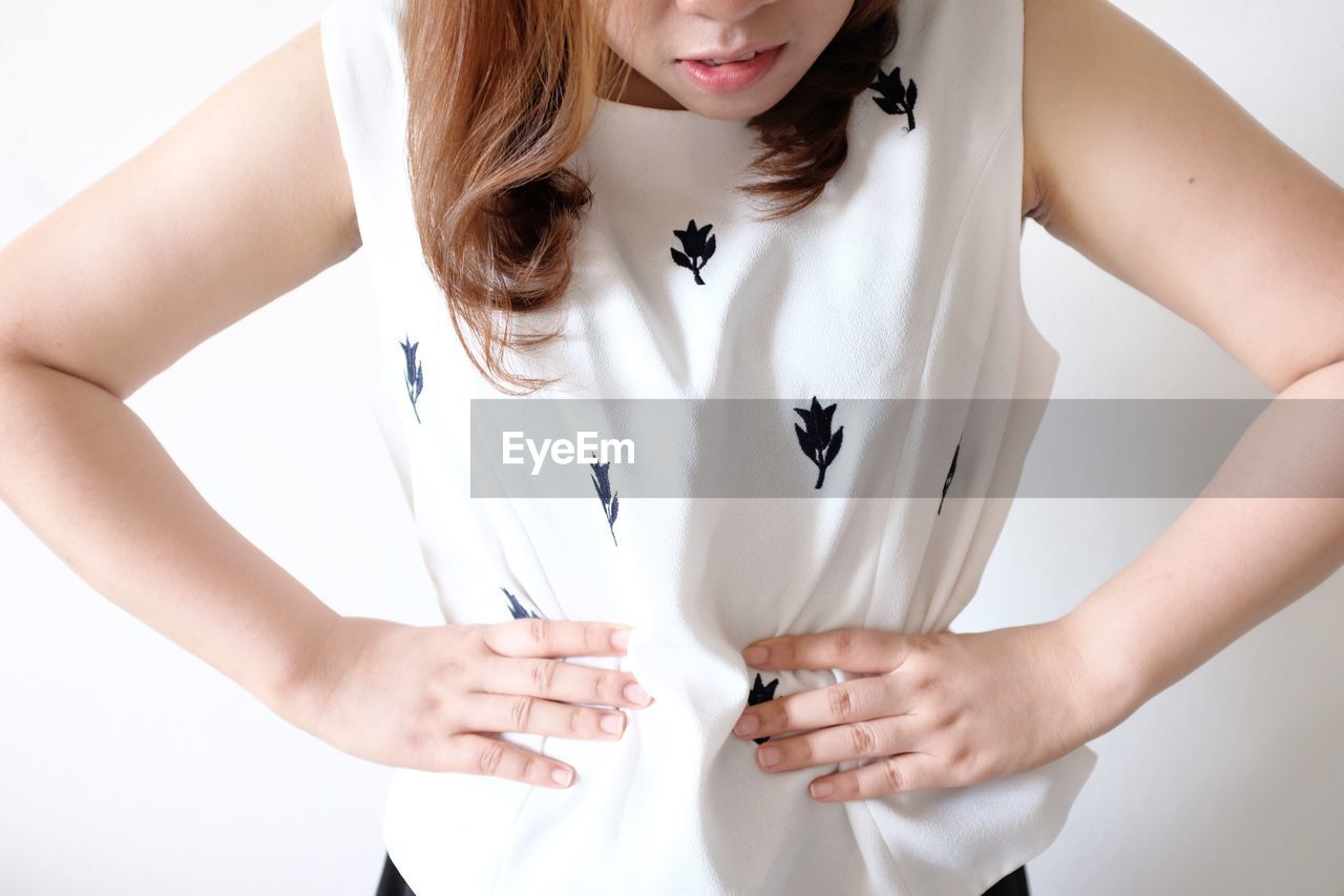 Midsection of woman with hands on stomach standing against white background