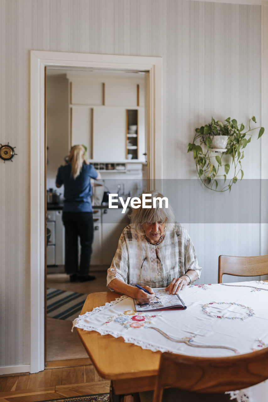 Senior woman solving puzzle while sitting on dining table at home