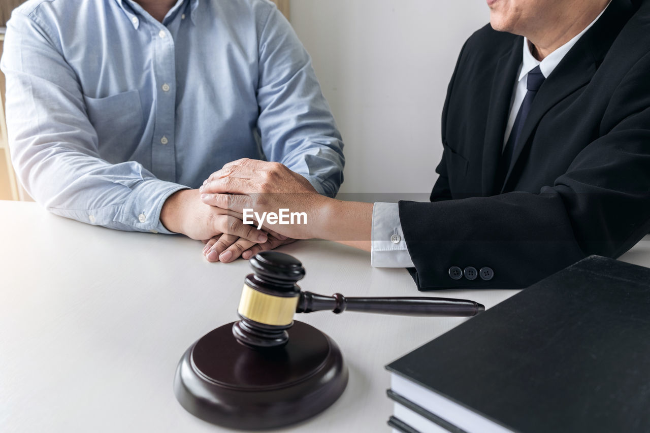 Close-up of lawyer and client with holding hands at desk in courtroom