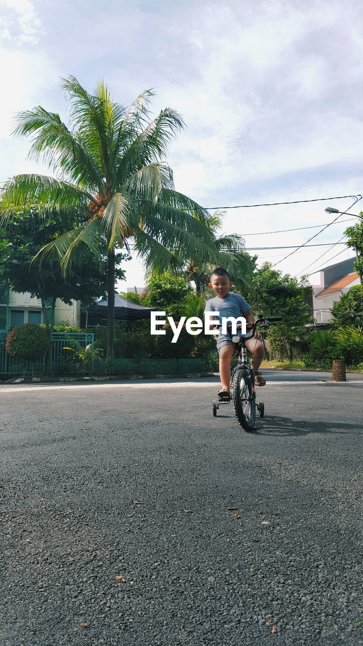 Boy riding bicycle on road against sky