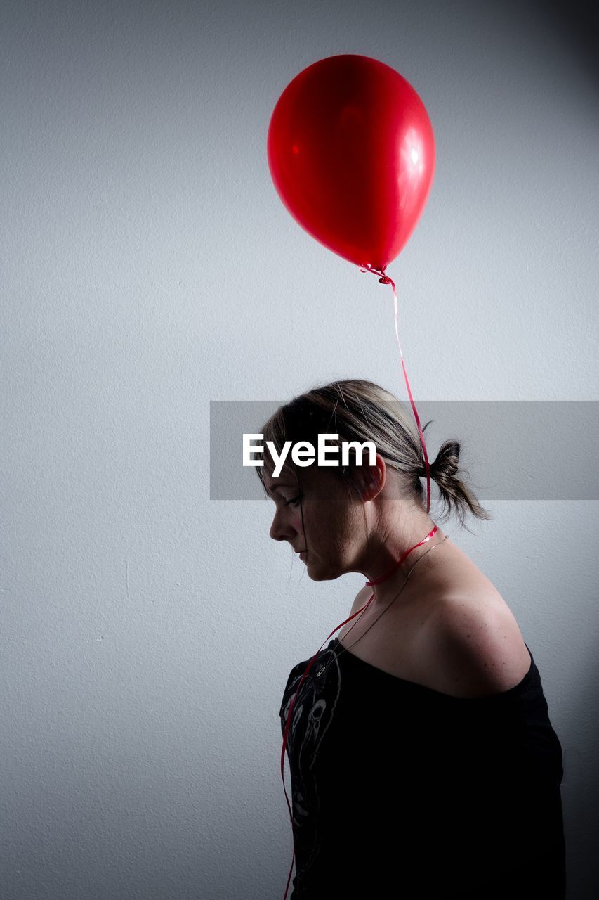 Side view of woman with red balloon against wall