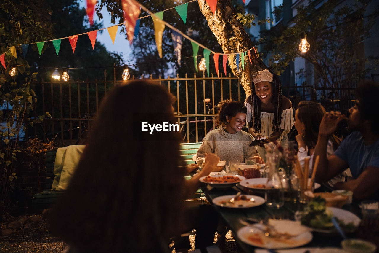 Smiling young woman showing mobile phone to female friends at table during dinner party