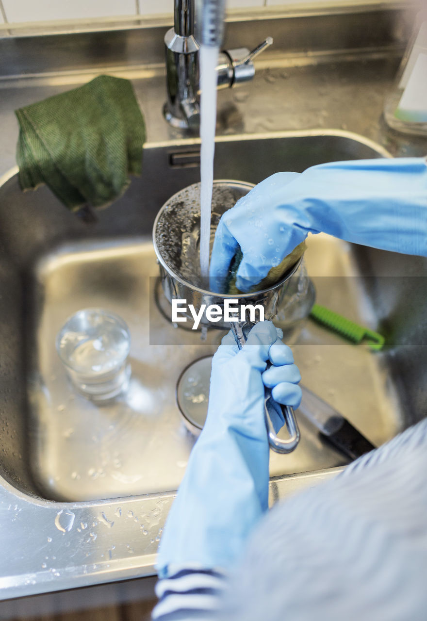 Cropped image of woman washing sauce pan at sink in kitchen