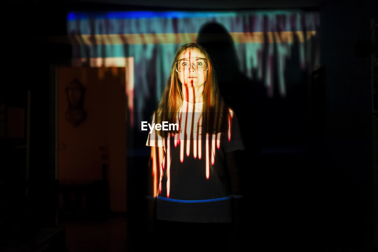 Mid adult woman standing in light reflection at home during pandemic