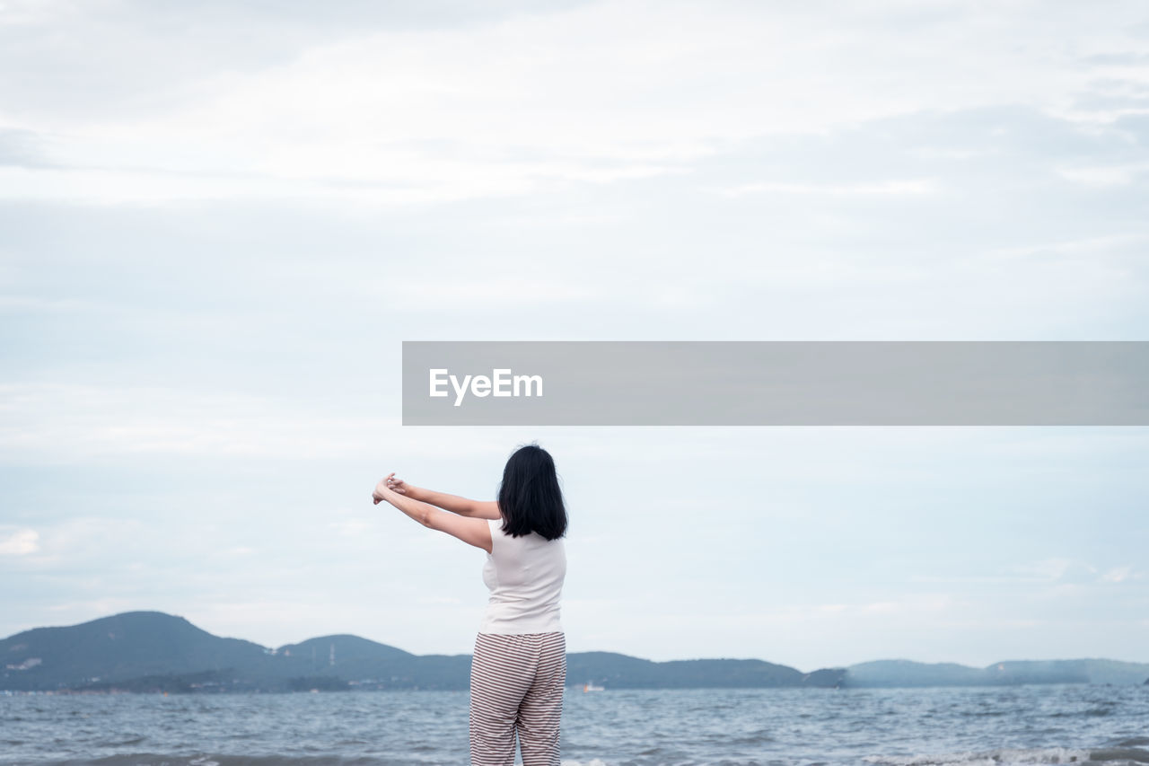 Rear view of woman standing by sea against sky