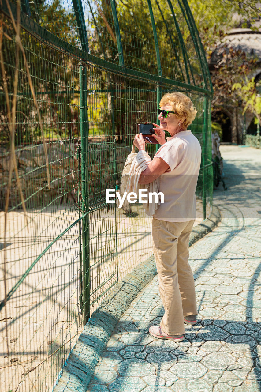 Elderly woman with mobile smartphone taking photo in zoo