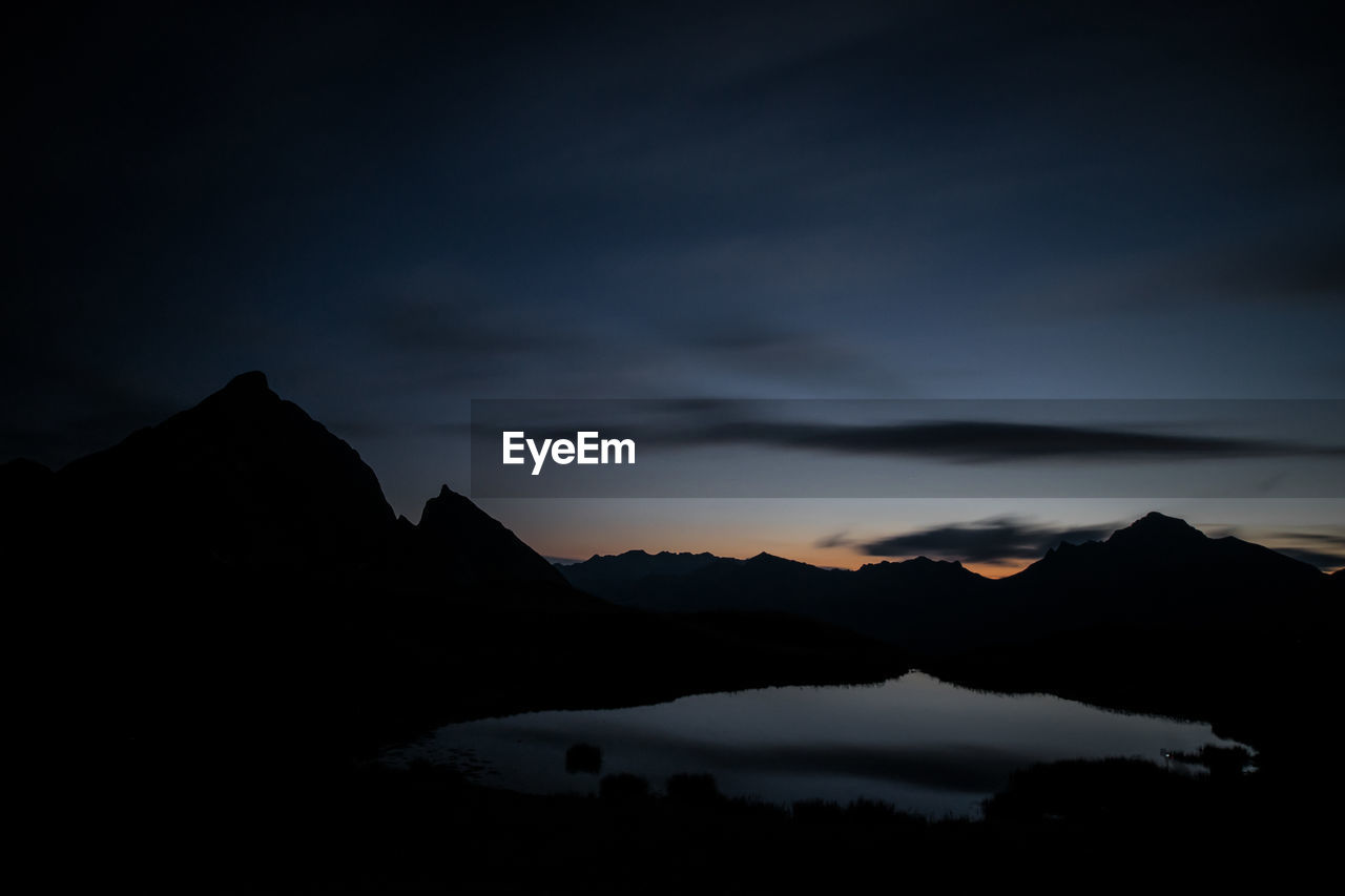 Scenic view of silhouette mountains by lake against sky at night