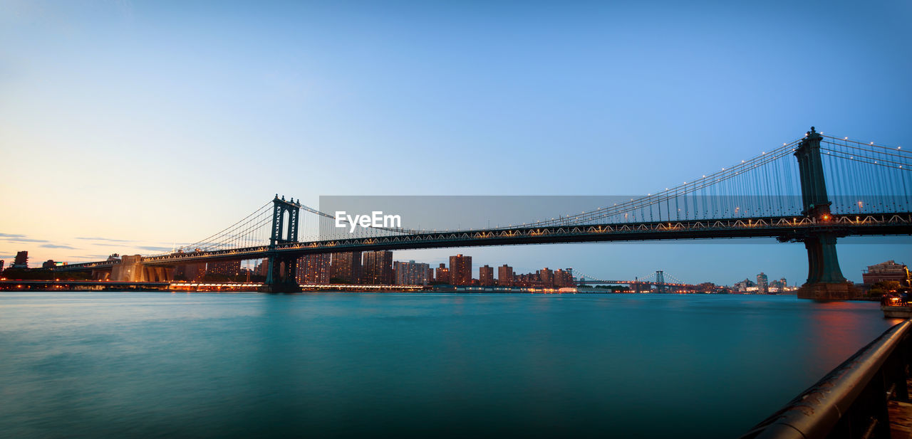 Low angle view of manhattan bridge over river against clear sky during sunset