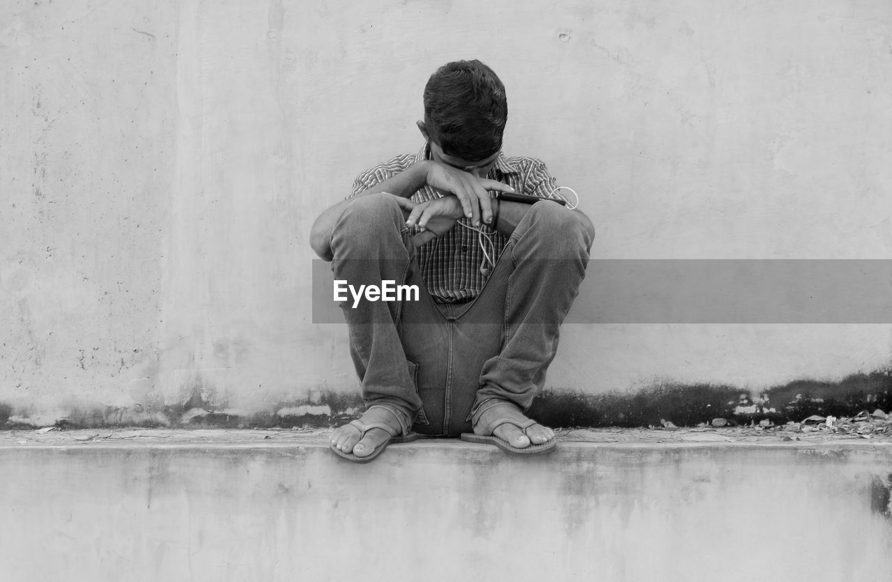 REAR VIEW OF BOY SITTING ON WALL