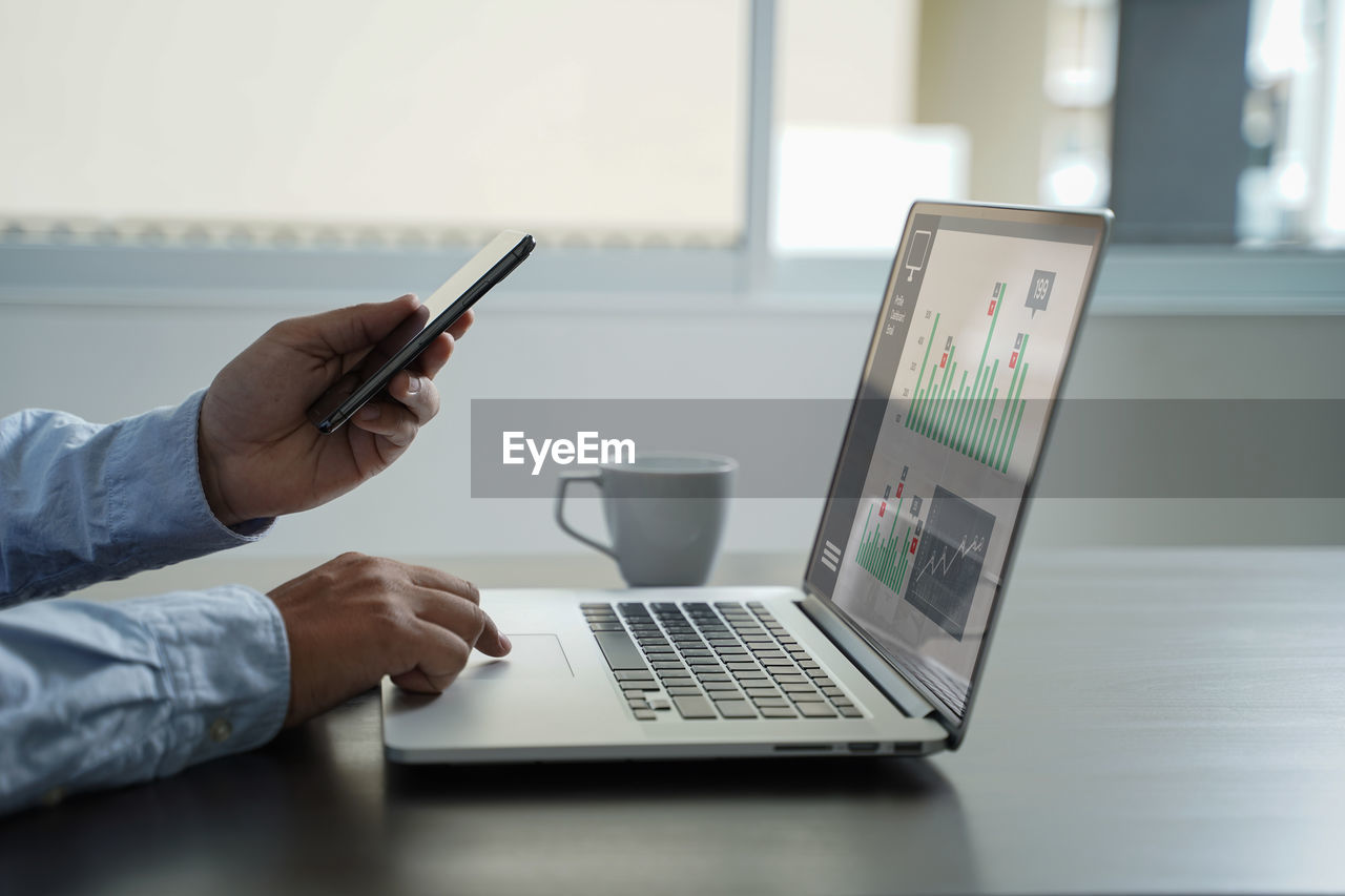 Cropped hands of businessman using phone and laptop in office