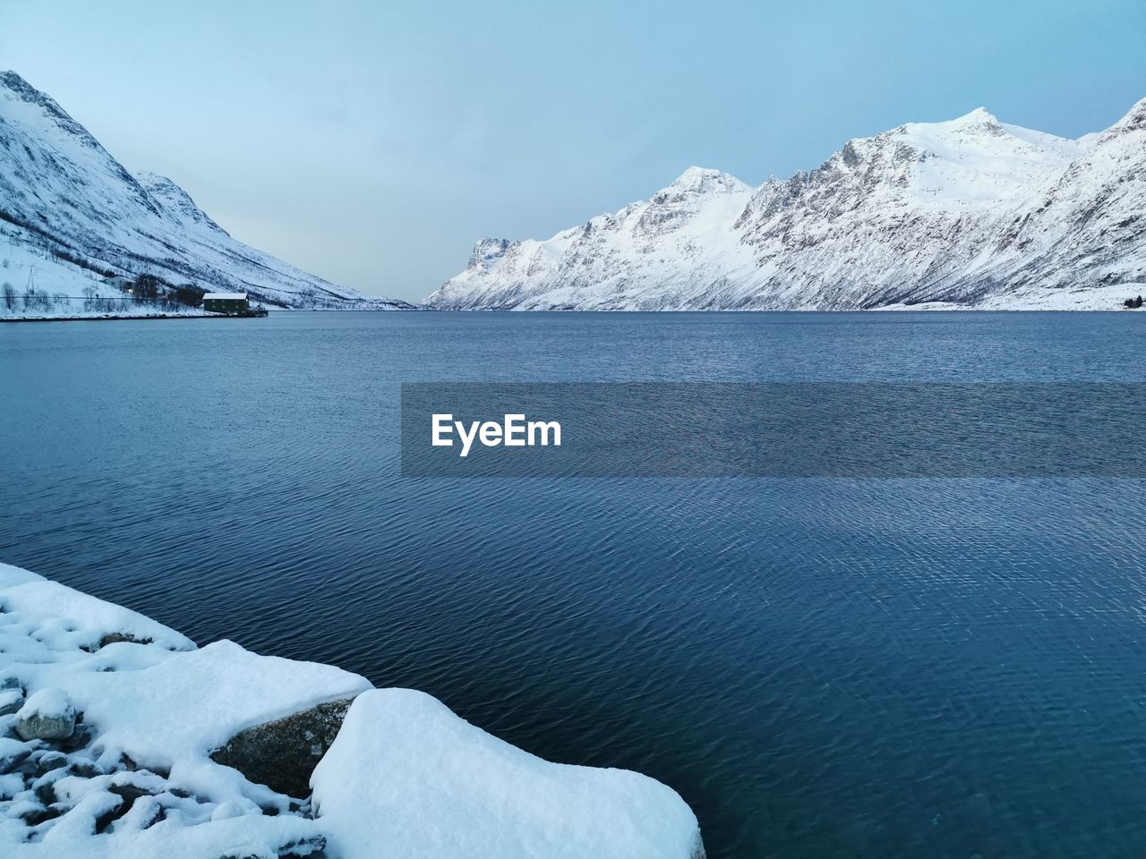 Frozen lake by snowcapped mountains against sky