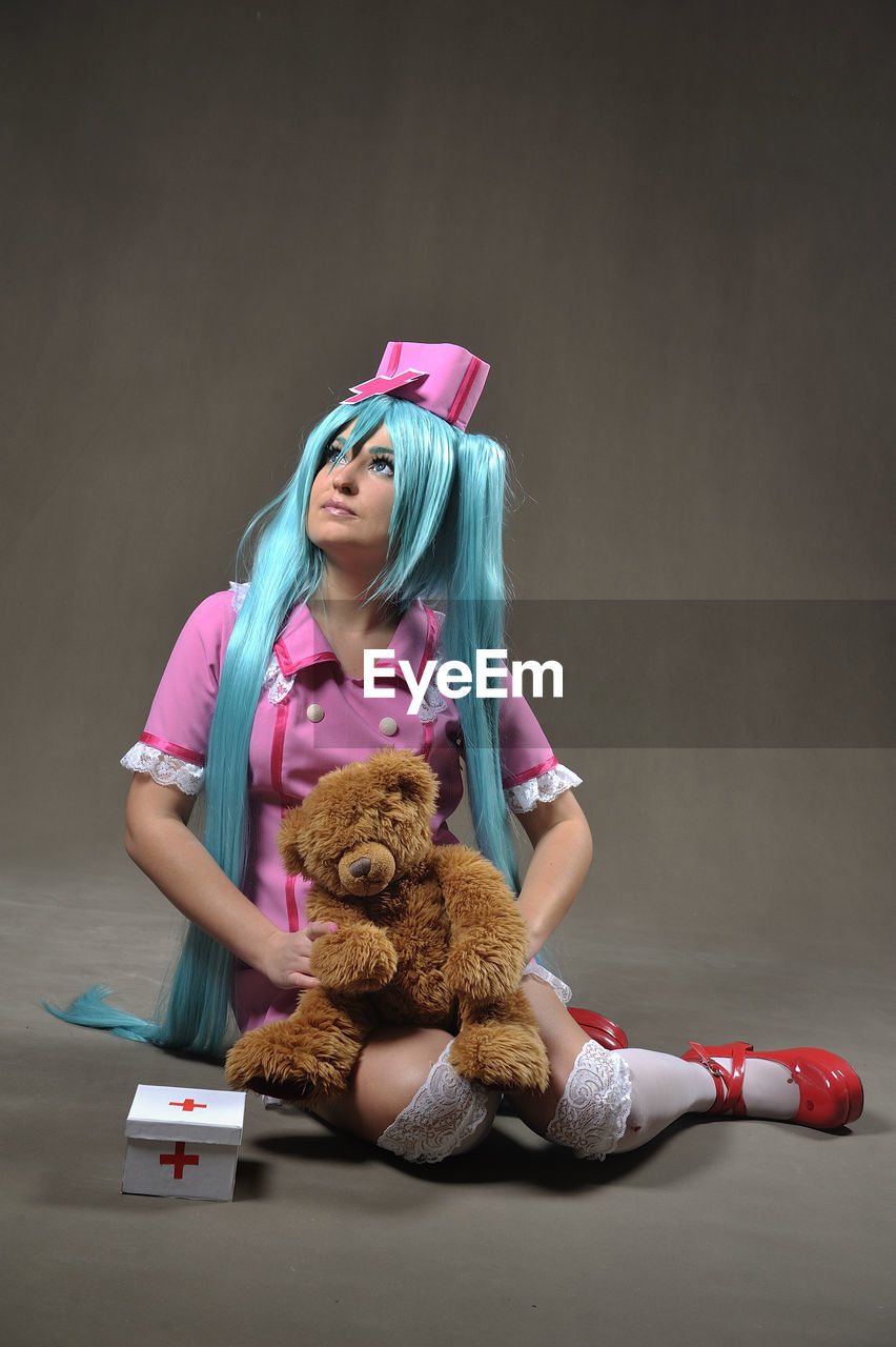 Young nurses with long blue hair holding teddy bear against gray background