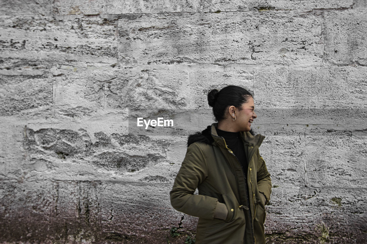 one person, wall - building feature, standing, young adult, lifestyles, looking, leisure activity, clothing, men, architecture, looking away, casual clothing, adult, wall, day, waist up, person, temple, outdoors, jacket, contemplation, three quarter length, built structure, coat, nature, spring, side view