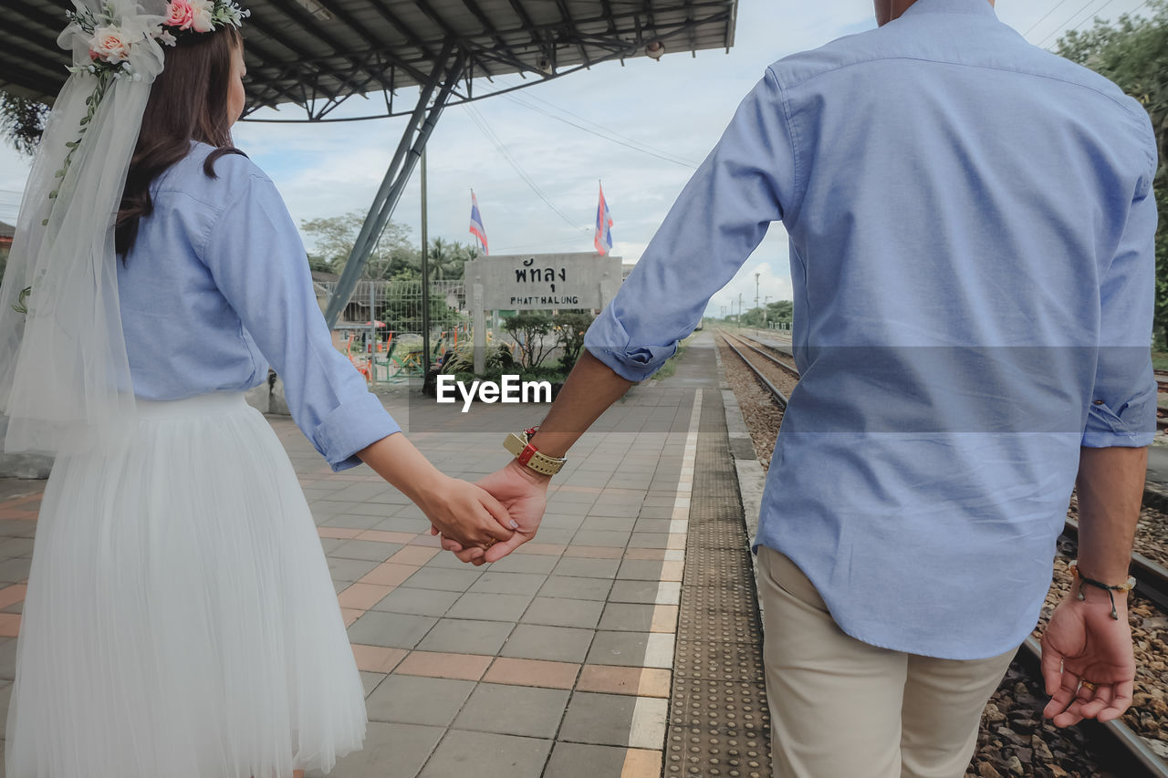 REAR VIEW OF MAN AND WOMAN WALKING ON CITY