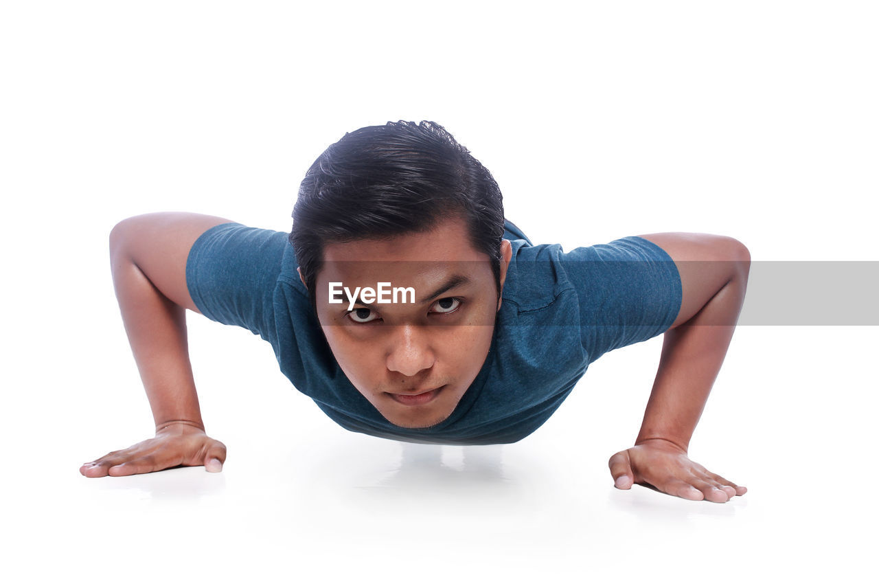 Portrait of young man doing push-ups against white background