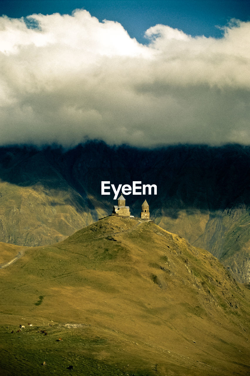 Gergeti trinity church on mountain against cloudy sky