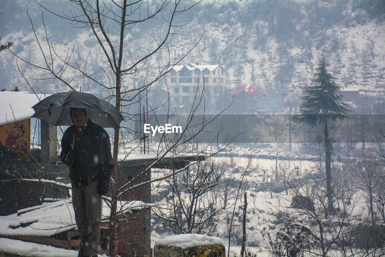 MAN ON SNOW COVERED TREE AGAINST MOUNTAIN