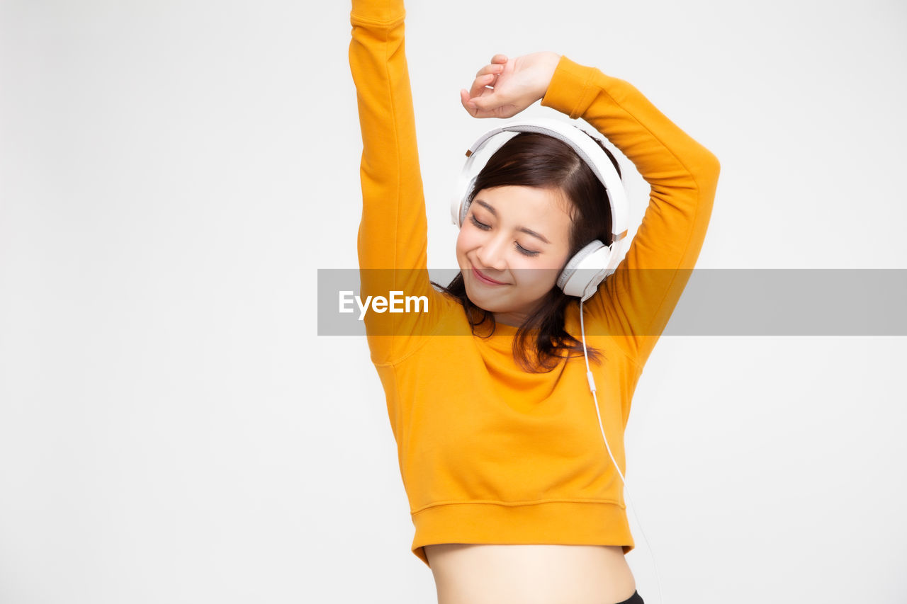 Smiling young woman listening music over headphones against white background