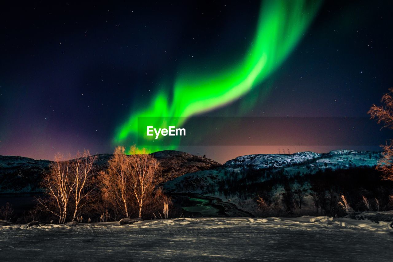 Aurora borealis over landscape against sky at night
