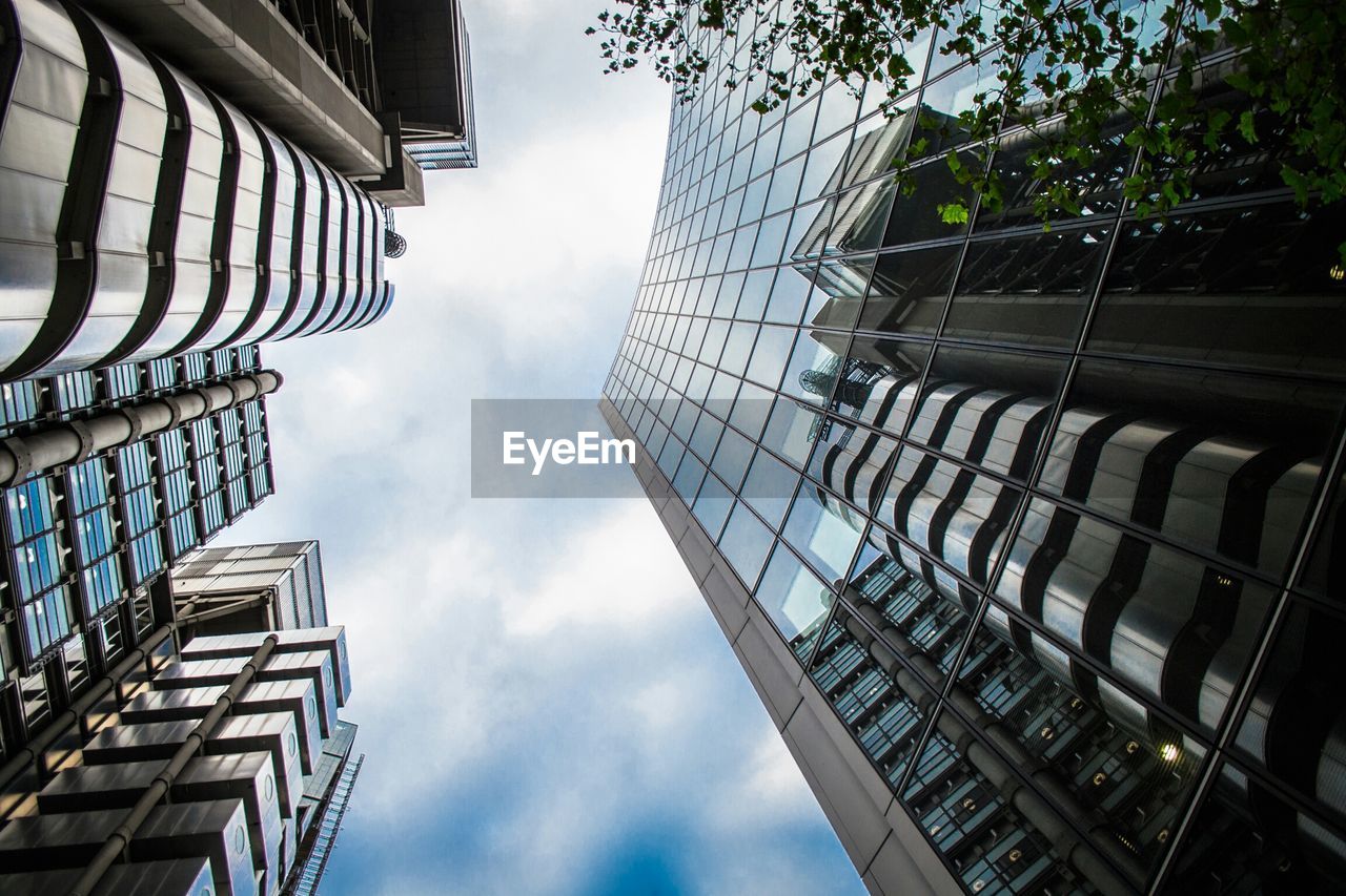 Directly below shot of modern buildings against cloudy sky in city