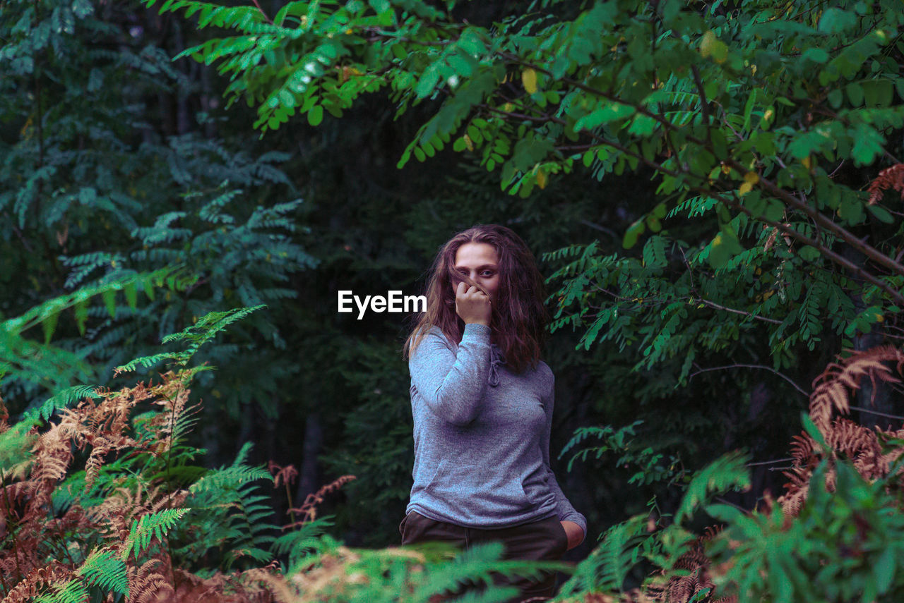 Portrait of woman standing amidst trees at forest