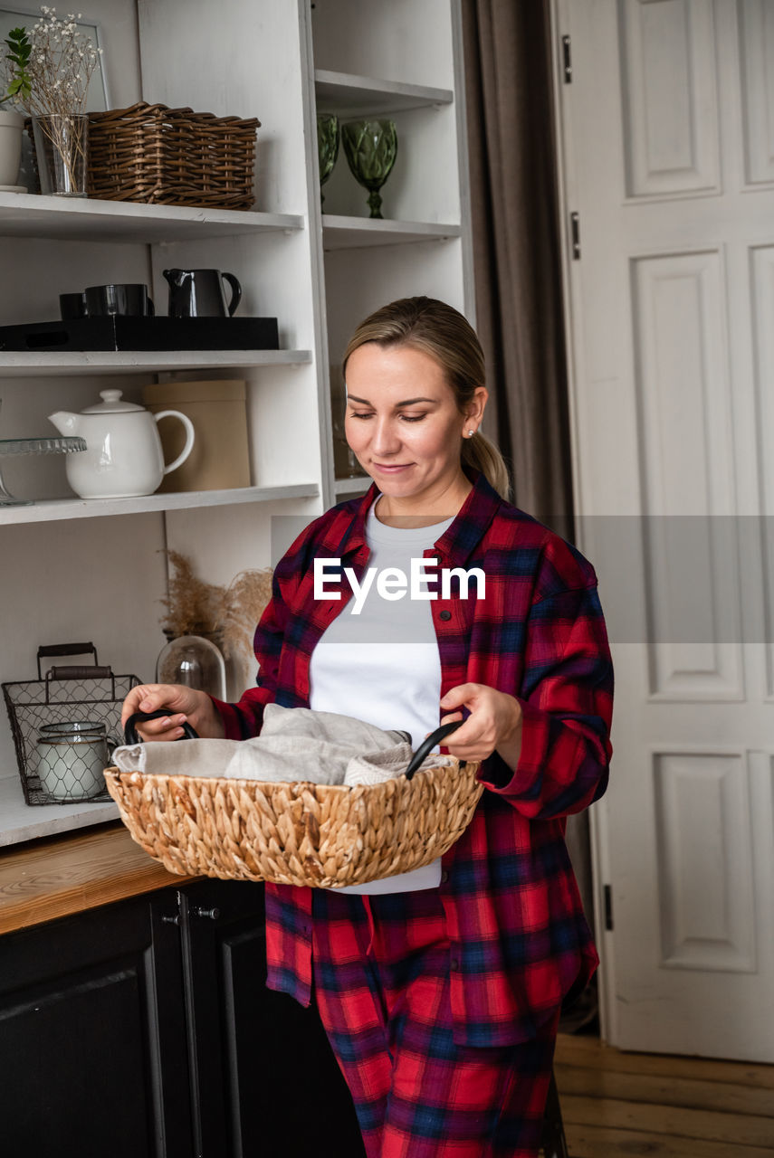 Attractive young blonde with a basket in her hands in front of her cozy kitchen. home style concept