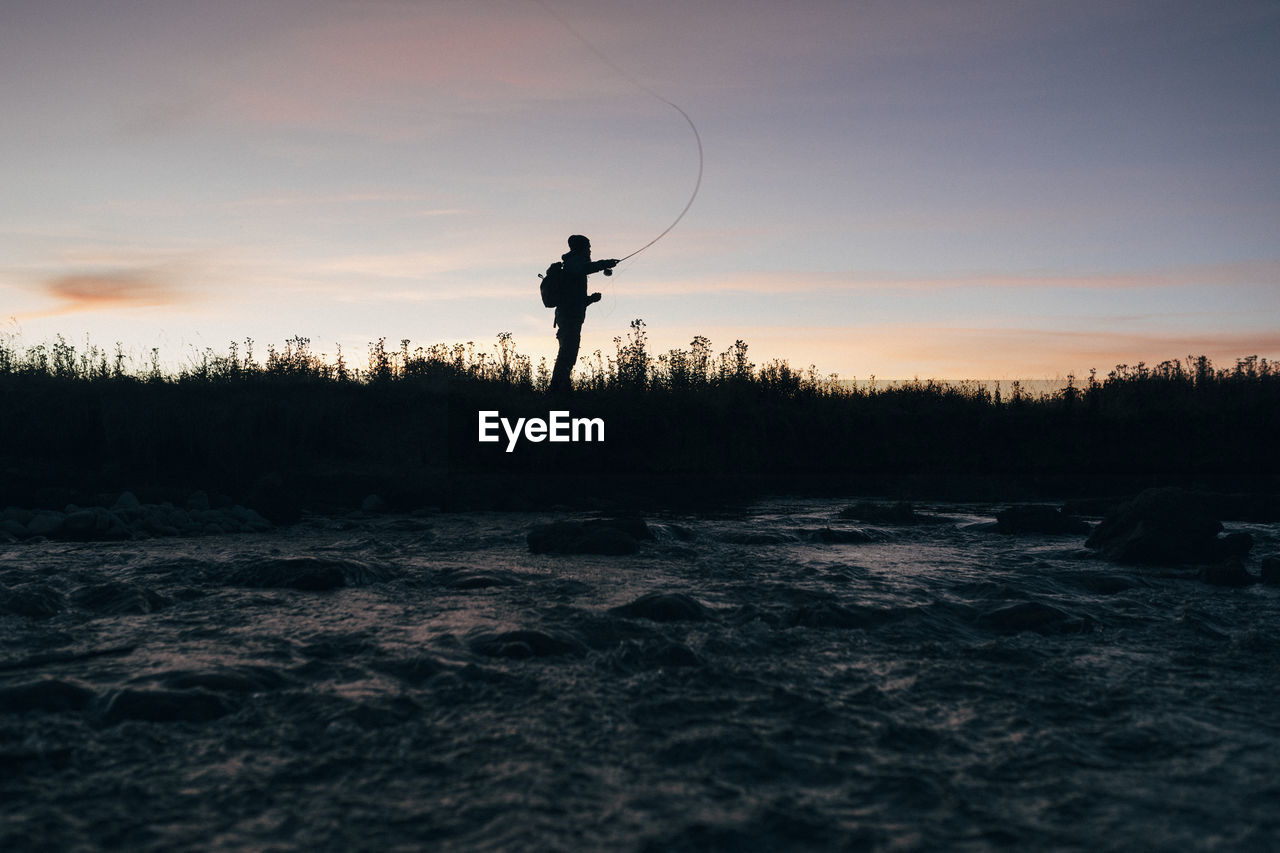 Silhouette of man fishing against sky during sunset