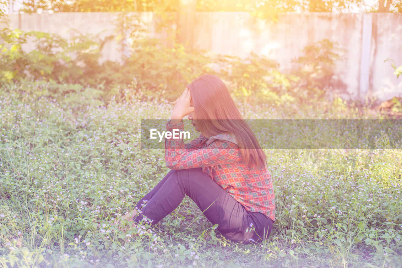 SIDE VIEW OF WOMAN SITTING ON FIELD DURING SUNNY DAY