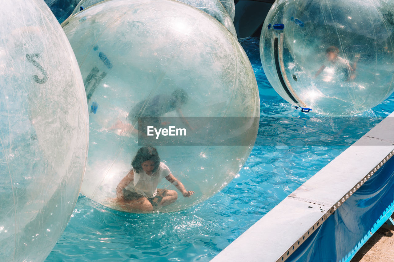 Woman sitting in zorb ball floating on swimming pool