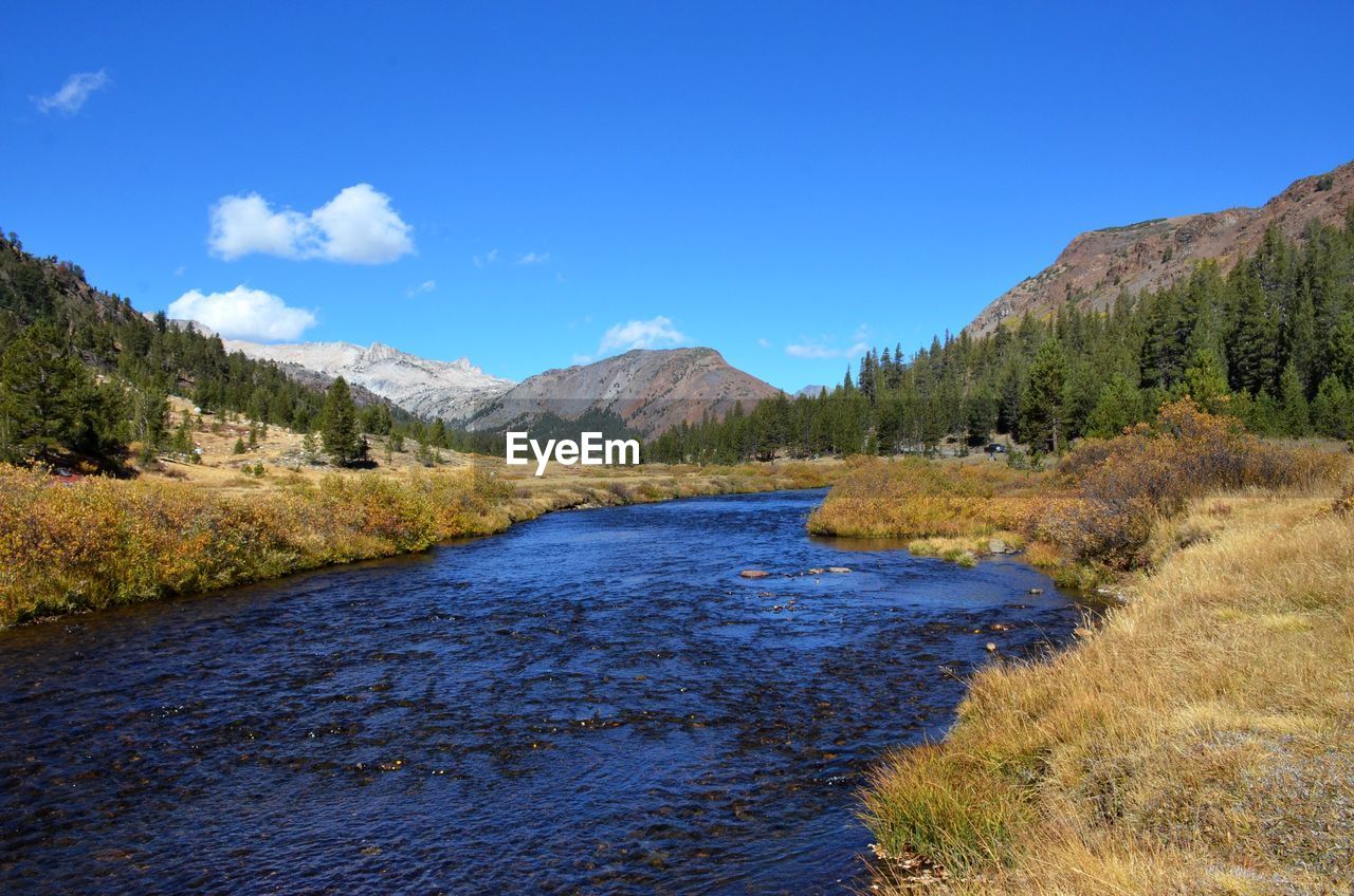 Scenic view of calm river surrounded by mountains against blue sky