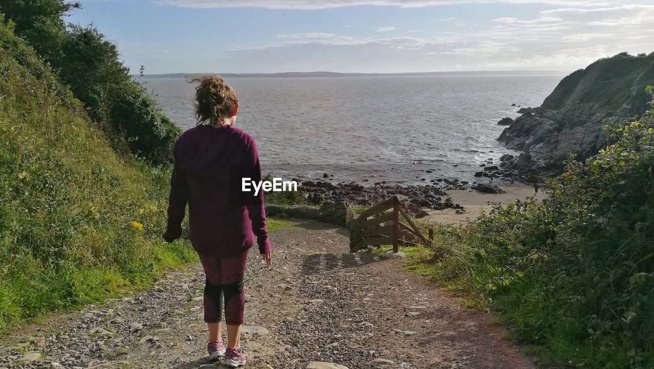 Rear view of woman walking on footpath against sea