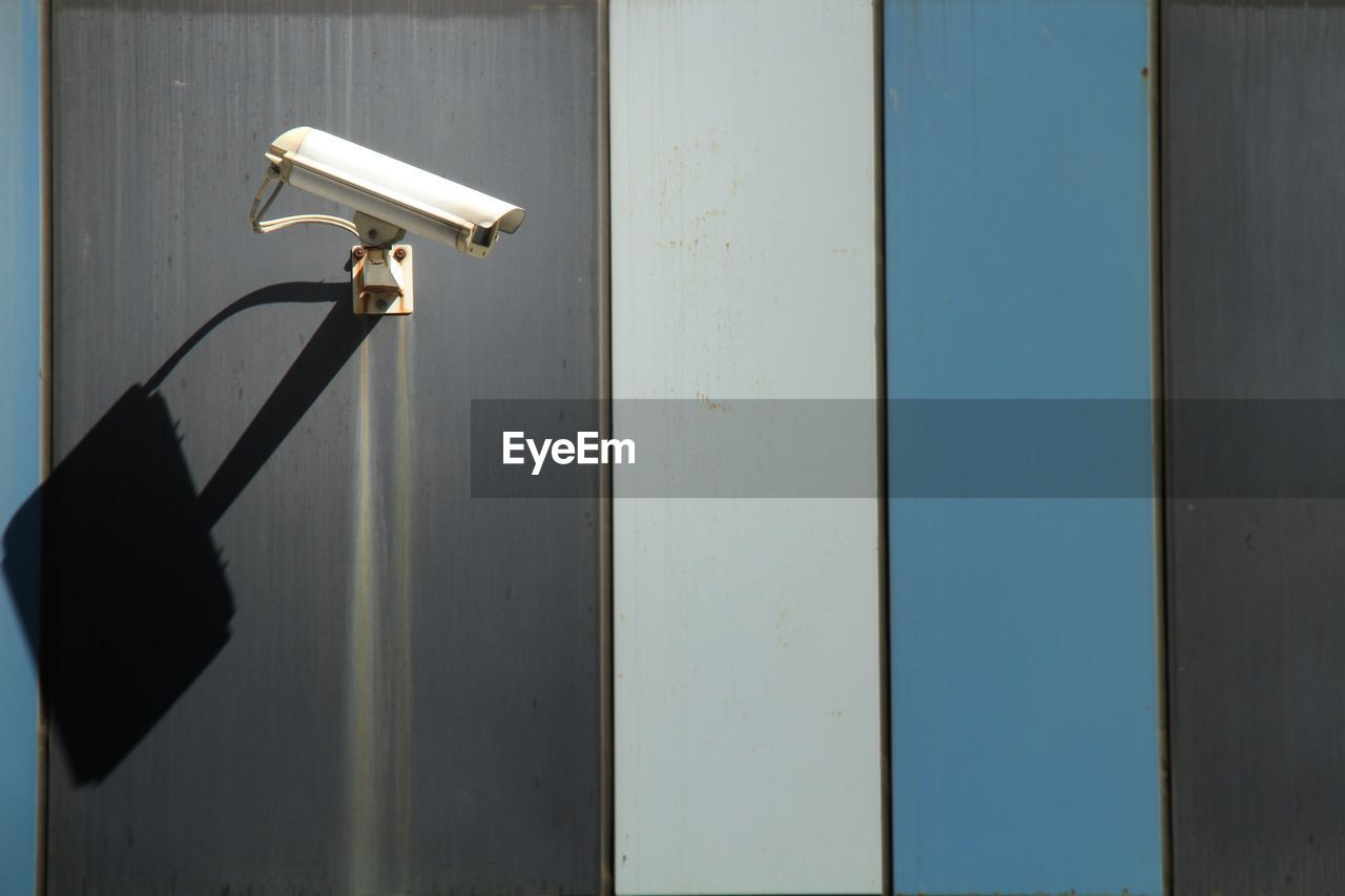 Security camera mounted on exterior building wall, casting shadow in sunlight