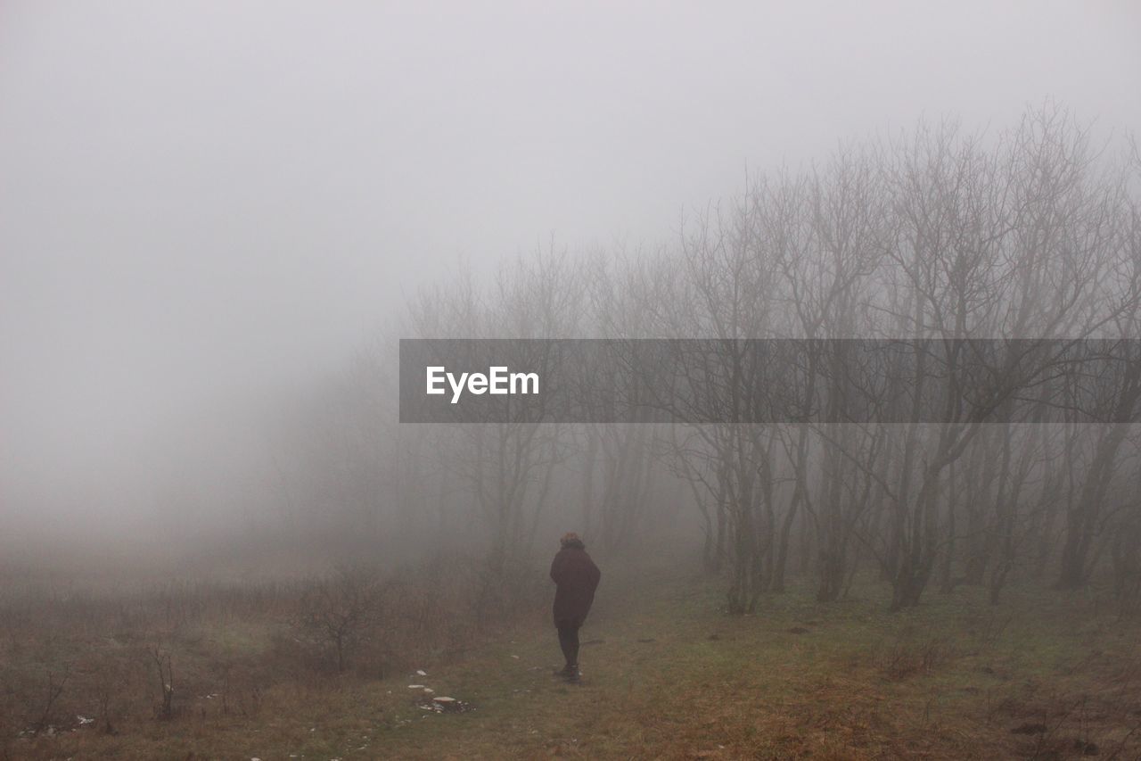 REAR VIEW OF A MAN WALKING ON FOGGY WEATHER