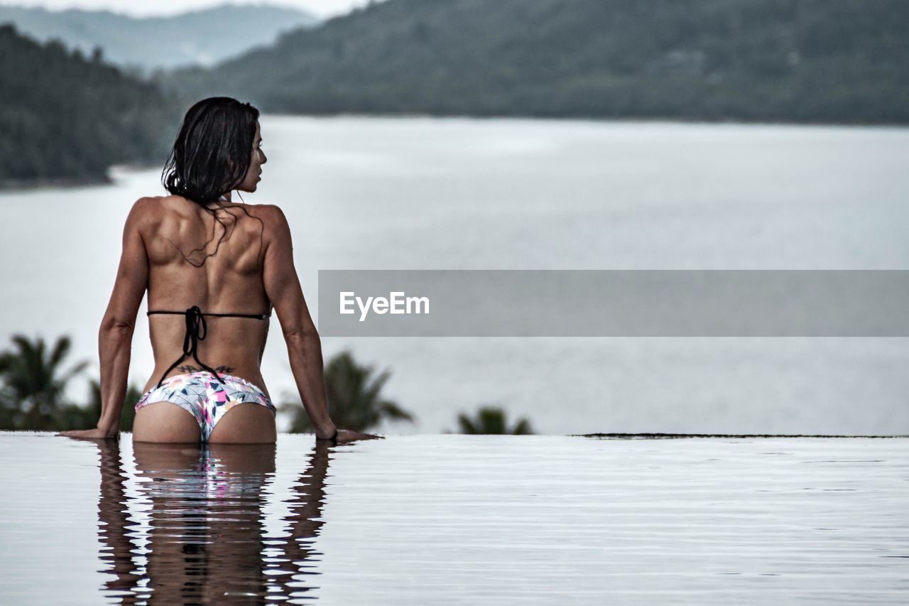 Rear view of mid adult woman wearing bikini swimming in infinity pool