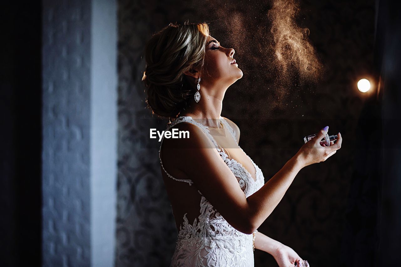 Side view of female model spraying perfume in darkroom