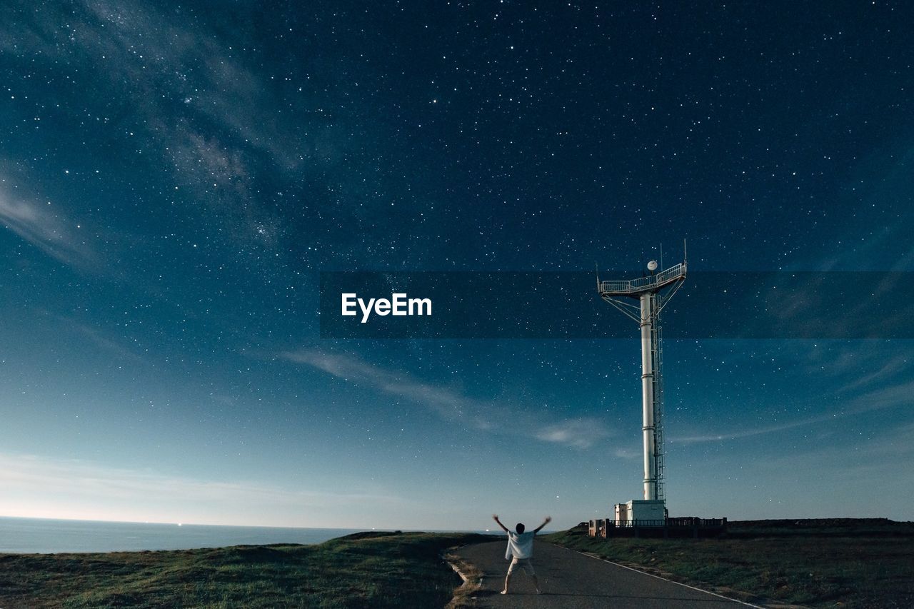 Rear view of man standing by communication tower against star field at dusk