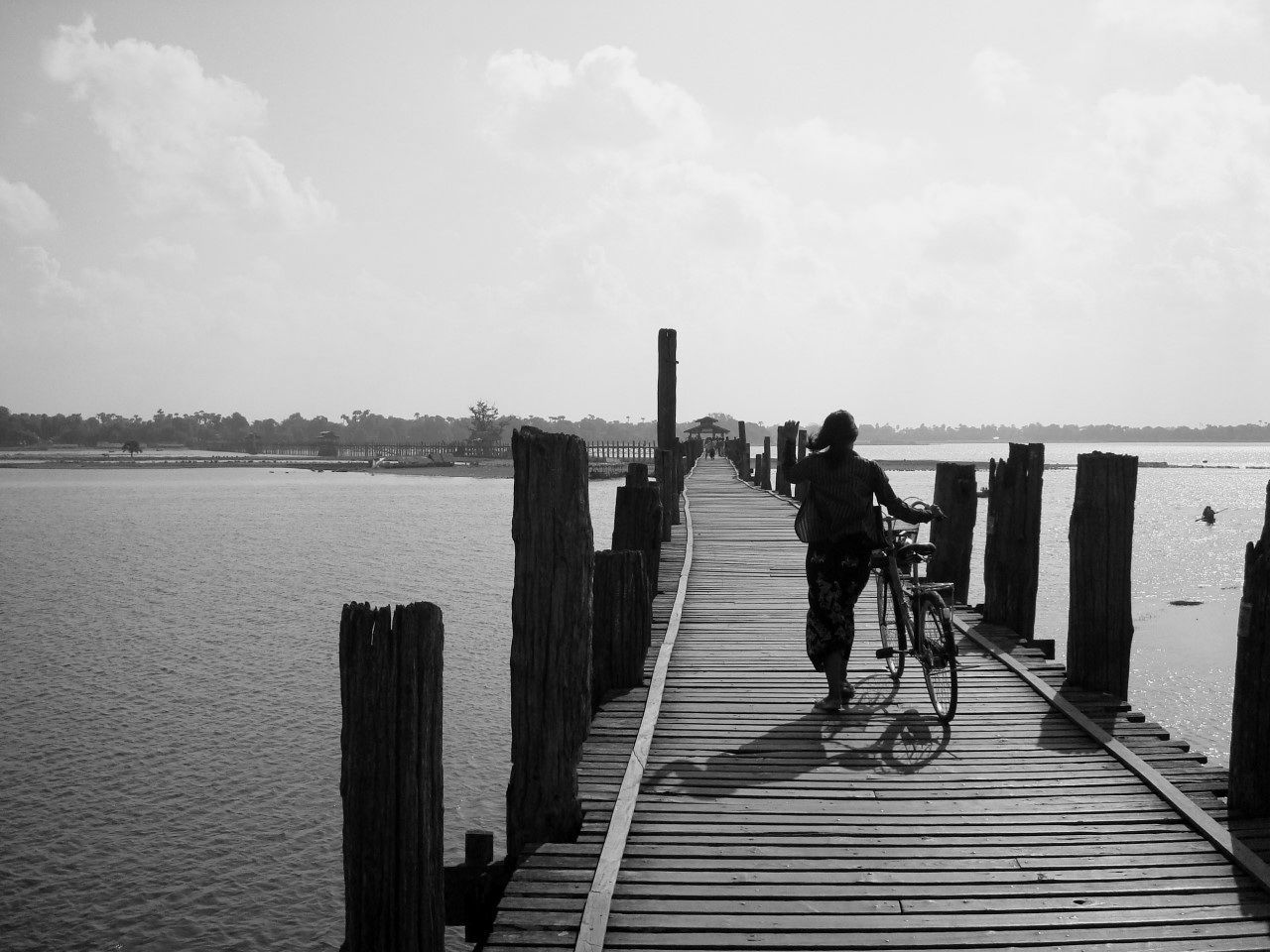 Rear view of woman walking with bicycle on wooden footbridge over river against sky