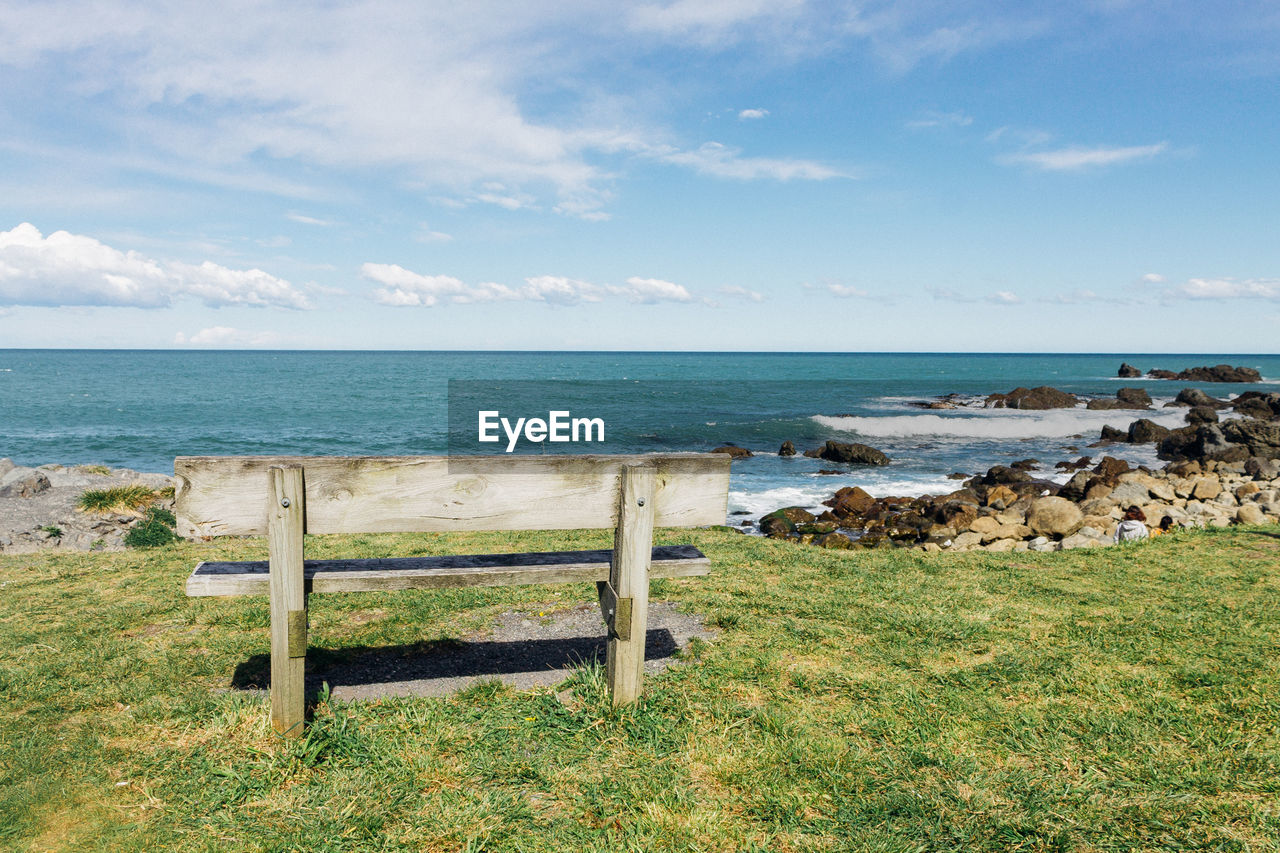 Empty bench by rocks against sea