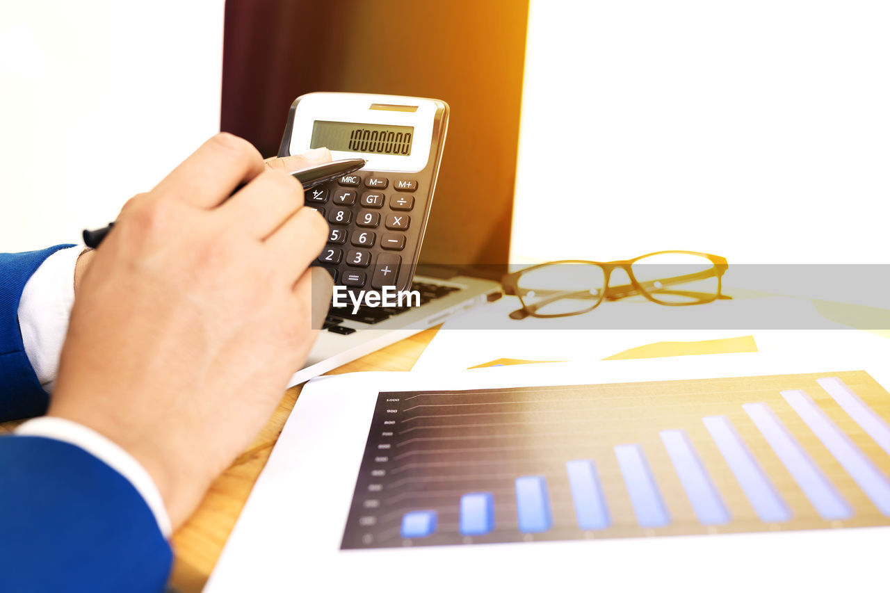 Midsection of man showing calculator on table in office