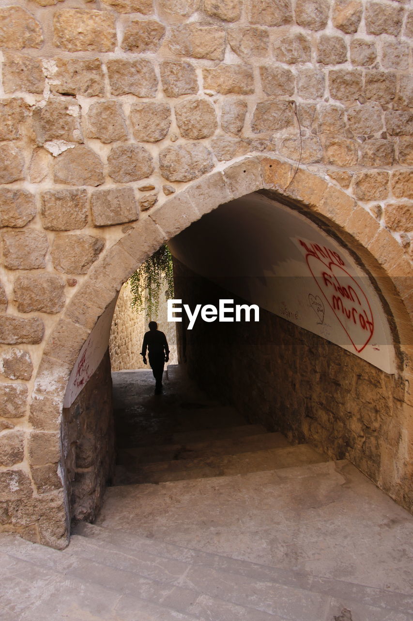 MAN WALKING BY BUILDING WALL