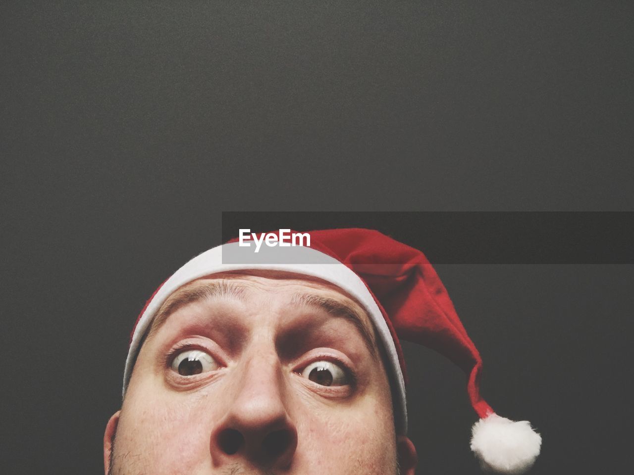 Cropped image of surprised man wearing santa hat against black background