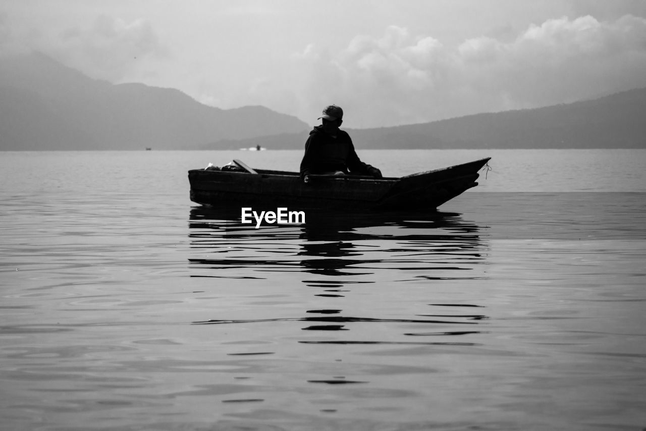 SILHOUETTE MAN SITTING ON BOAT AGAINST SKY