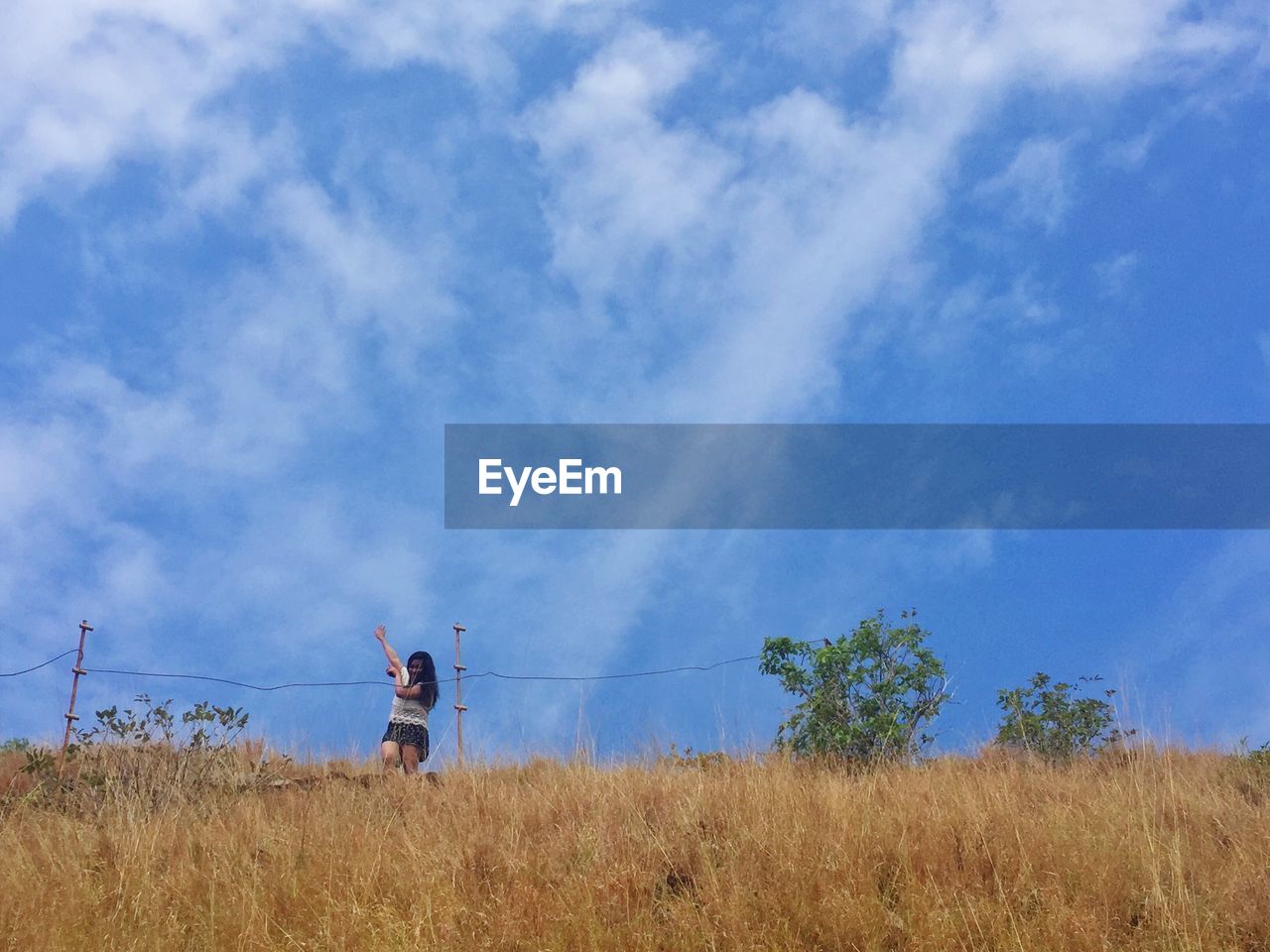 Low angle view of woman dancing on grassy field against cloudy sky