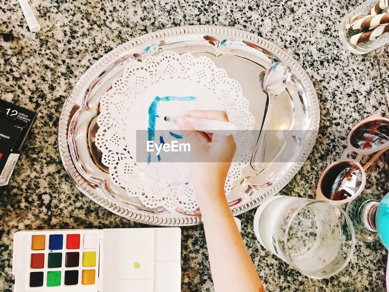 Cropped hand holding paintbrush by various objects on table