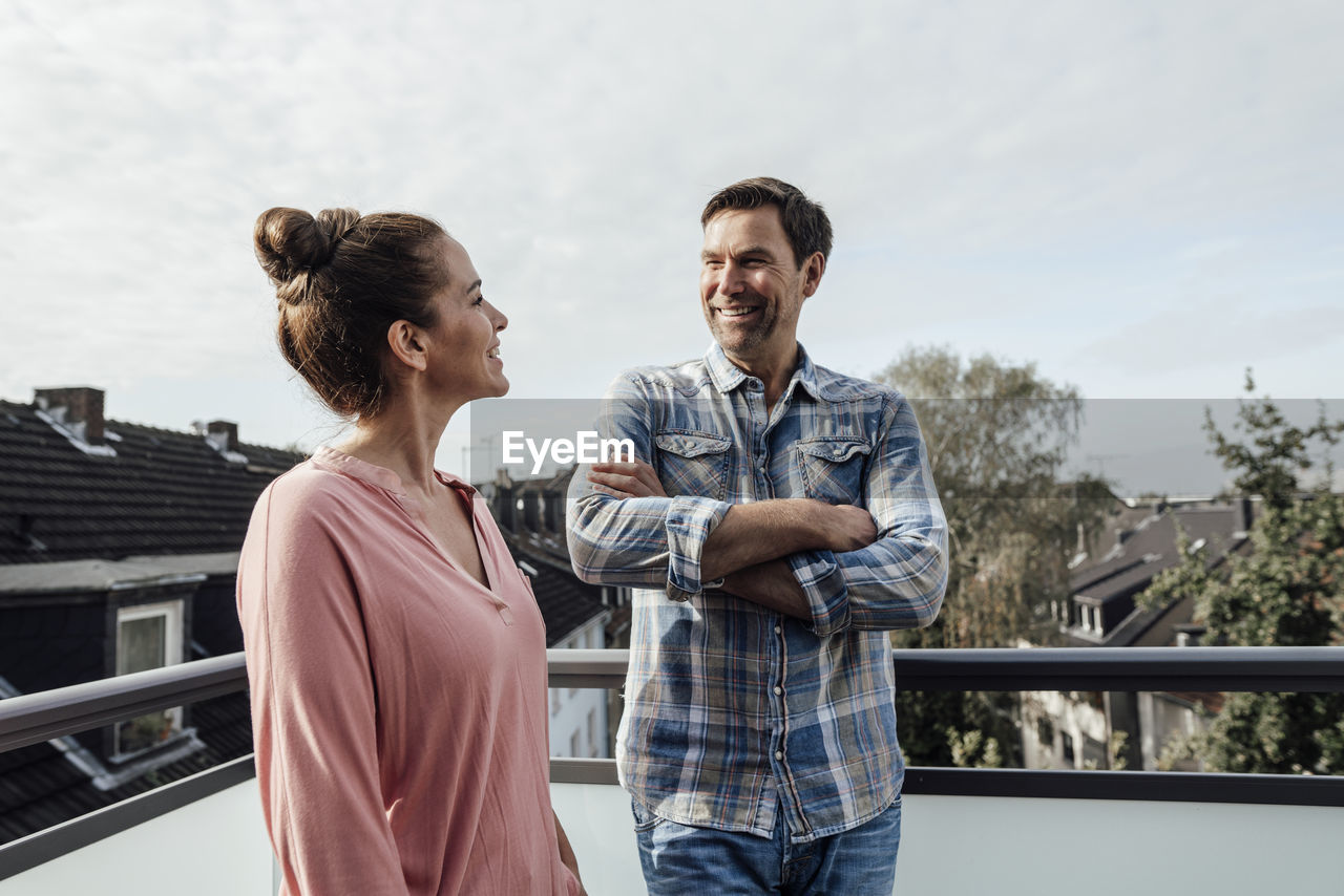 Mature man with arms crossed smiling while looking at woman in balcony