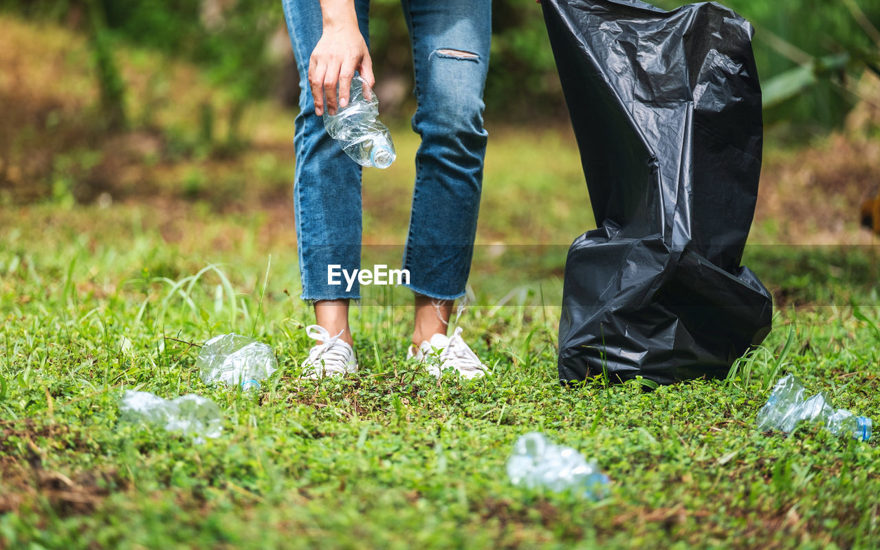 A female activist picking up garbage plastic bottles into a plastic bag in the park for recycling