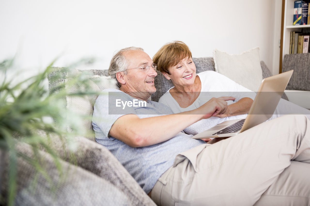 Senior couple at home sitting on couch using laptop