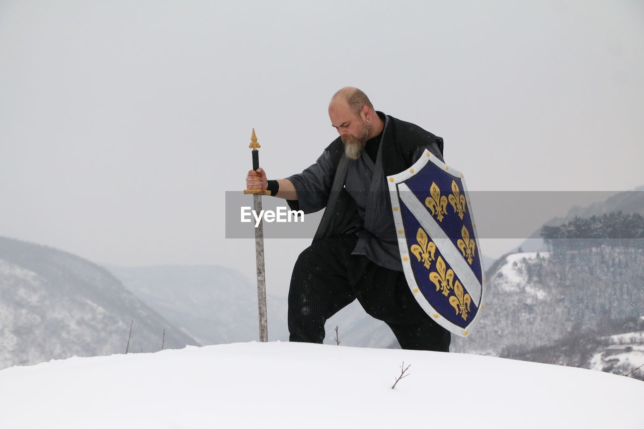 MAN HOLDING UMBRELLA ON SNOW COVERED MOUNTAIN AGAINST SKY