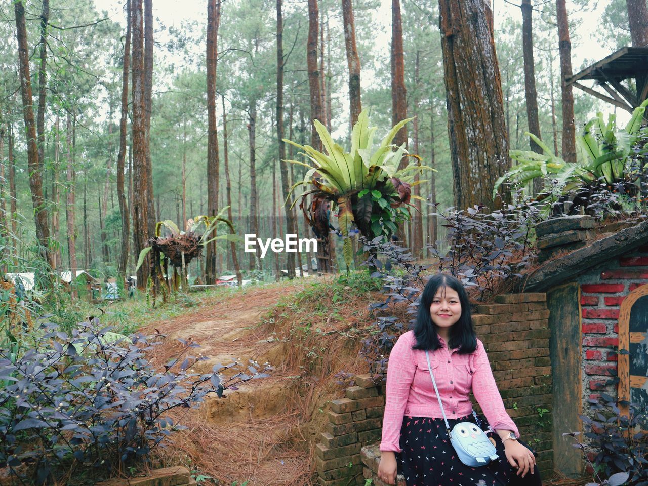 PORTRAIT OF A SMILING YOUNG WOMAN STANDING IN FOREST